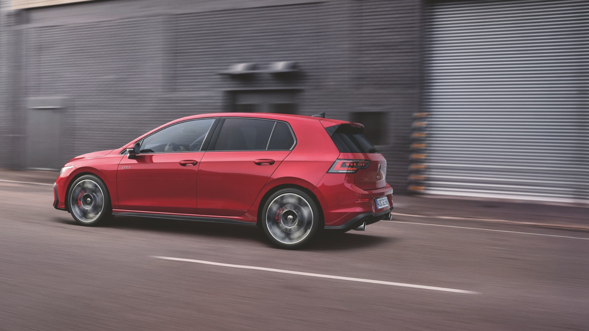 A red Volkswagen Golf GTI in motion, highlighting its dual chrome exhaust outlets.