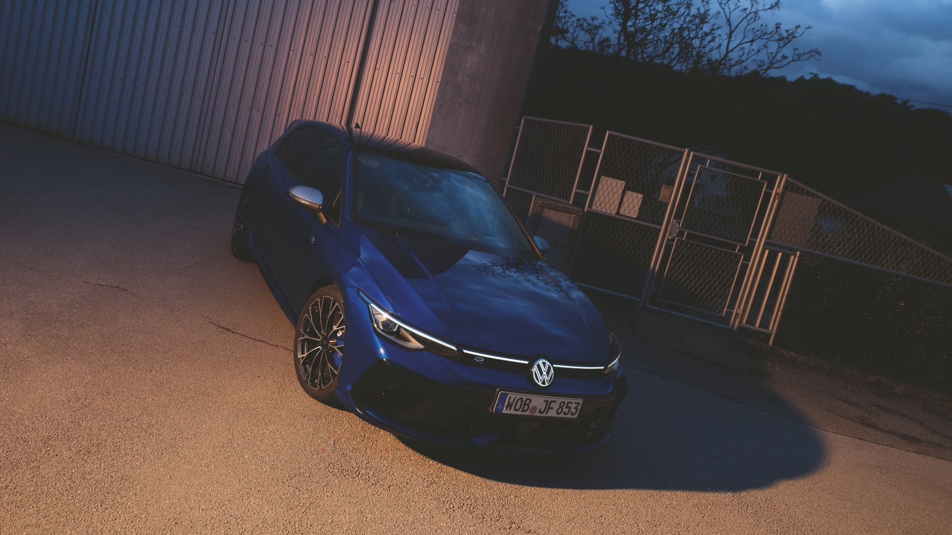 A blue Volkswagen Golf R with high-performance brakes, parked in front of a large building at dusk.