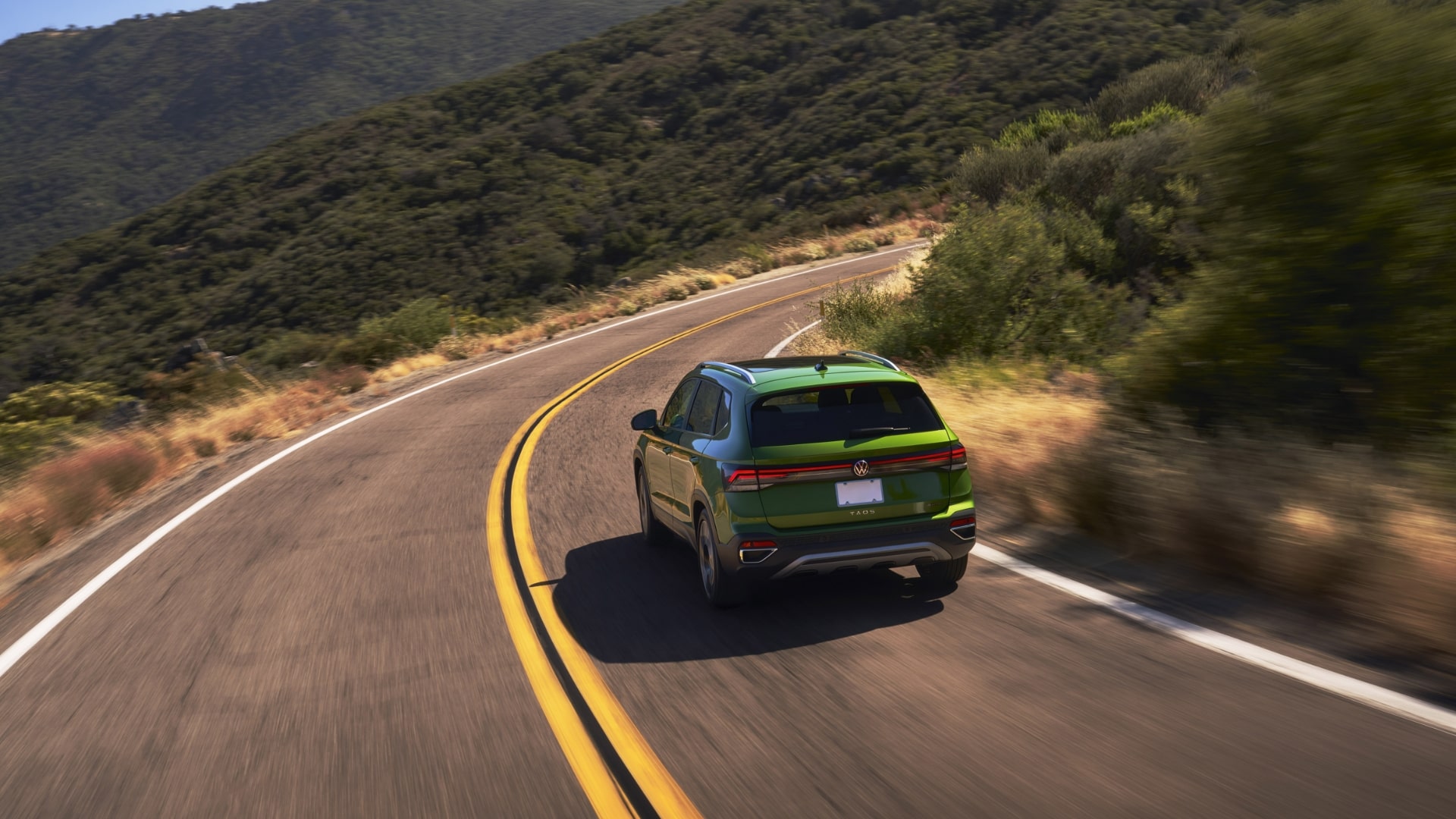 2025 Volkswagen Taos in motion on a curving road through a mountain landscape.